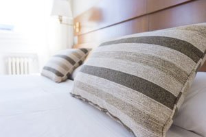 Weißes Bett auf dem zwei gestreifte Kissen liegen.